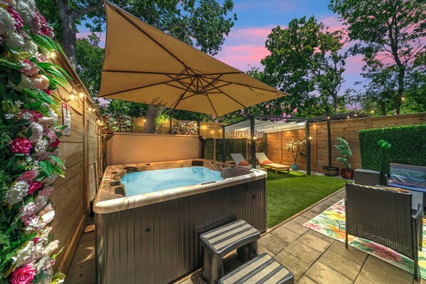 Een hottub met treden, omgeven door een houten terras en een grote parasol.
