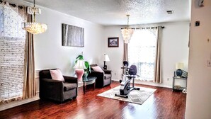 A living room with hardwood flooring, two armchairs, a standing lamp, a painting, and a stationary exercise bike. - A fully furnished home within walking distance of downtown Mansfield (Mansfield)