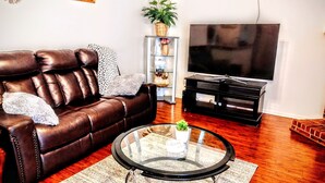 A living room with a leather sofa, a glass coffee table, a TV, and a wooden floor. - A fully furnished home within walking distance of downtown Mansfield (Mansfield)