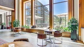 A spacious indoor area with large windows, wooden furniture, and potted plants.