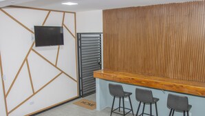 Un espace d’accueil avec un mur recouvert de panneaux en bois, un téléviseur à écran plat fixé au mur et trois tabourets de bar.