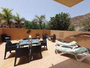 Relax in style with a dining table and lounge chairs amidst a serene hillside view.