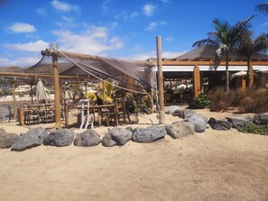Relax in a shaded outdoor seating area surrounded by palm trees and the beach.