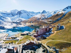 A mountainous area with a large body of water, several buildings, and a prominent hotel with multiple floors and a distinctive red and white facade. - 100m from resort center, 2nd floor, balcony, tv, ski locker, 53m², Tignes (Tignes)