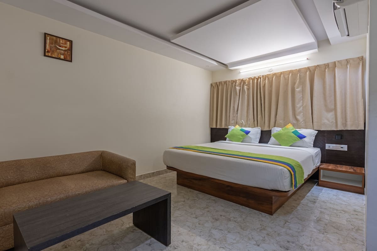 A hotel room with a bed, a sofa, a small table, and a painting on the wall.