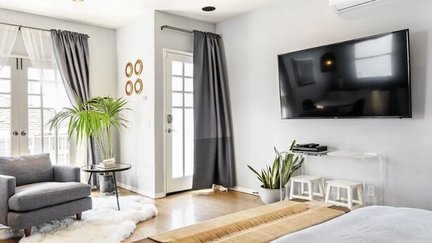 Et moderne hotelværelse med en stor seng, en grå lænestol, et fladskærms-tv og en potteplante.