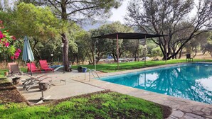 A backyard with a swimming pool, red lounge chairs, a pergola, and a stone pathway. - Hotel Rural Finca Liceo  (Mijares)