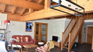 A cozy living room with a wooden ceiling, a red sofa, a wooden coffee table, and a staircase. - 3rd floor, balcony, fireplace or stove, tv, 110m², Pralognan-la-Vanoise (Pralognan-la-Vanoise)