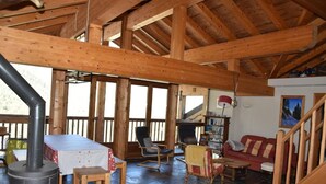A rustic wooden interior with a stone floor, a red sofa, a wooden table, and a fireplace. - 3rd floor, balcony, fireplace or stove, tv, 110m², Pralognan-la-Vanoise (Pralognan-la-Vanoise)