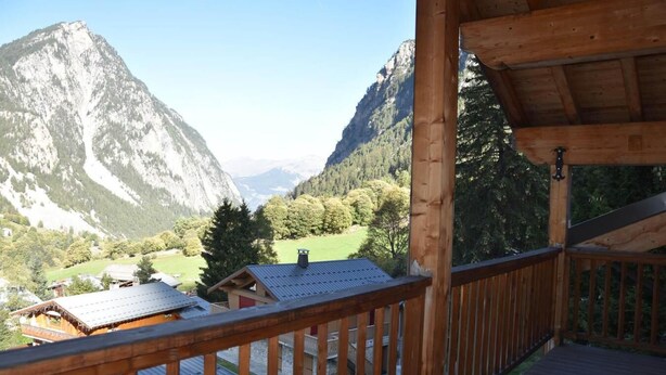 A wooden balcony with a view of a mountain landscape, including a prominent peak and a valley with buildings and trees. - 3rd floor, balcony, fireplace or stove, tv, 110m², Pralognan-la-Vanoise (Pralognan-la-Vanoise)