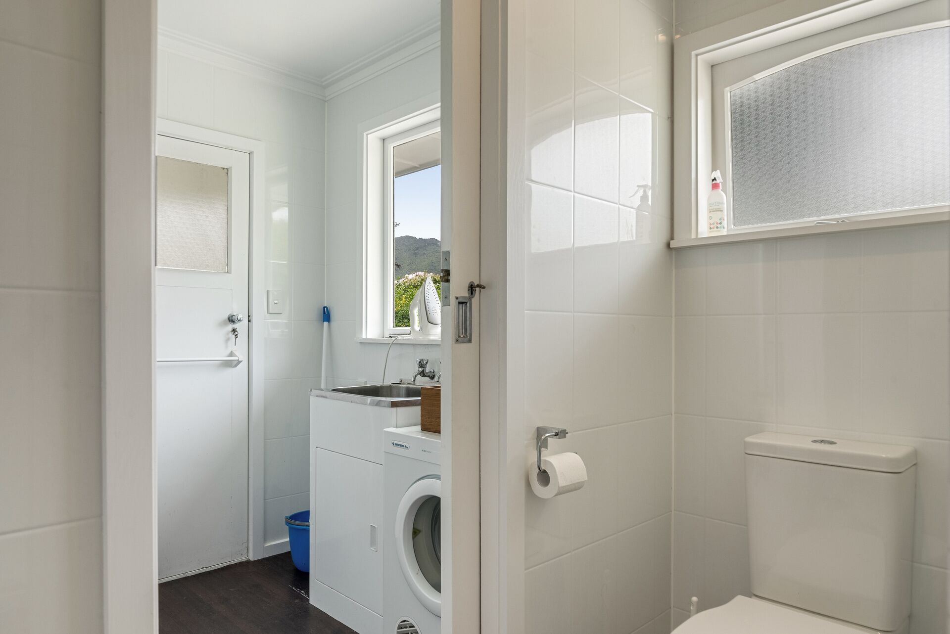 Une petite salle de bain équipée d’un lave-linge, de toilettes et d’une fenêtre donnant sur un espace verdoyant.