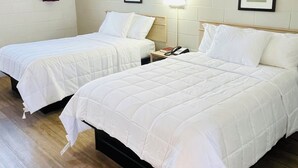 Dos camas individuales con ropa blanca, una mesita de noche con lámpara y un cuadro en la pared.