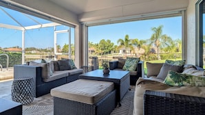 A sunlit patio with wicker furniture, a pool view, and a clear sky. - Luxury south facing waterfront home with heated salt pool and spa! (Cape Coral)