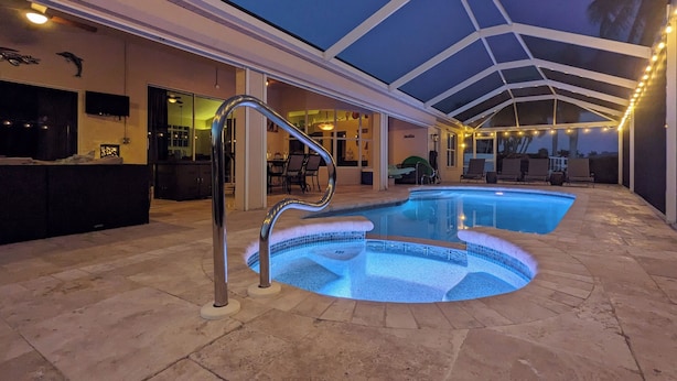 An indoor swimming pool with a glass ceiling, stone flooring, and a bar area with seating. - Luxury south facing waterfront home with heated salt pool and spa! (Cape Coral)