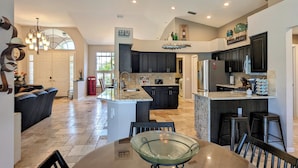A spacious kitchen with dark cabinets, a large island, and a dining area with a glass-top table. - Luxury south facing waterfront home with heated salt pool and spa! (Cape Coral)