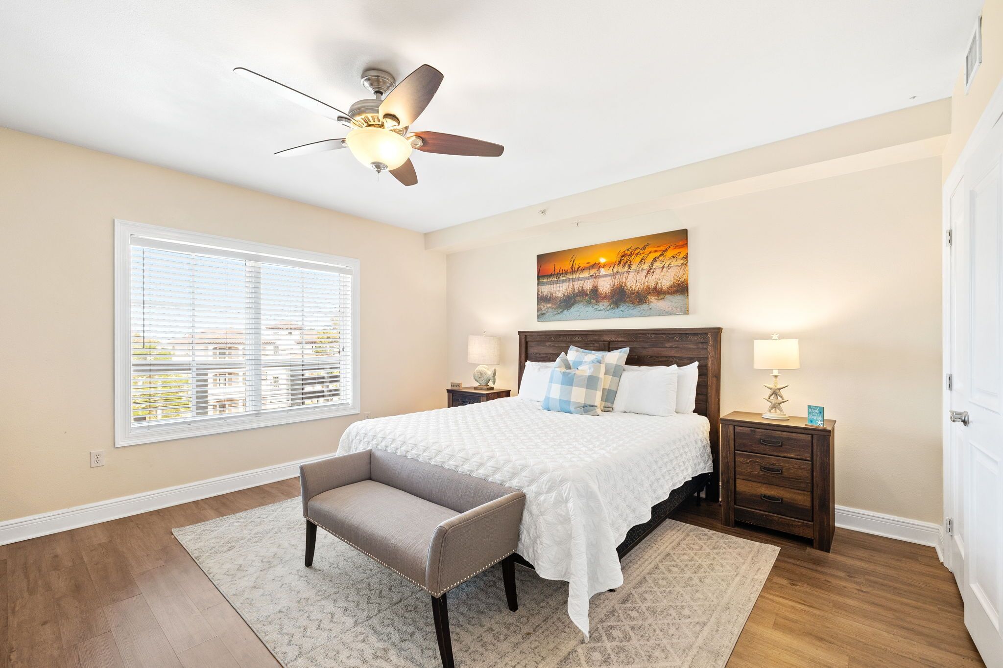 A bedroom with a bed, a chair, a nightstand, a lamp, a painting, and a window.
