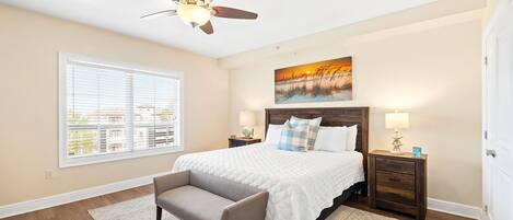 A bedroom with a bed, a chair, a nightstand, a lamp, a painting, and a window.