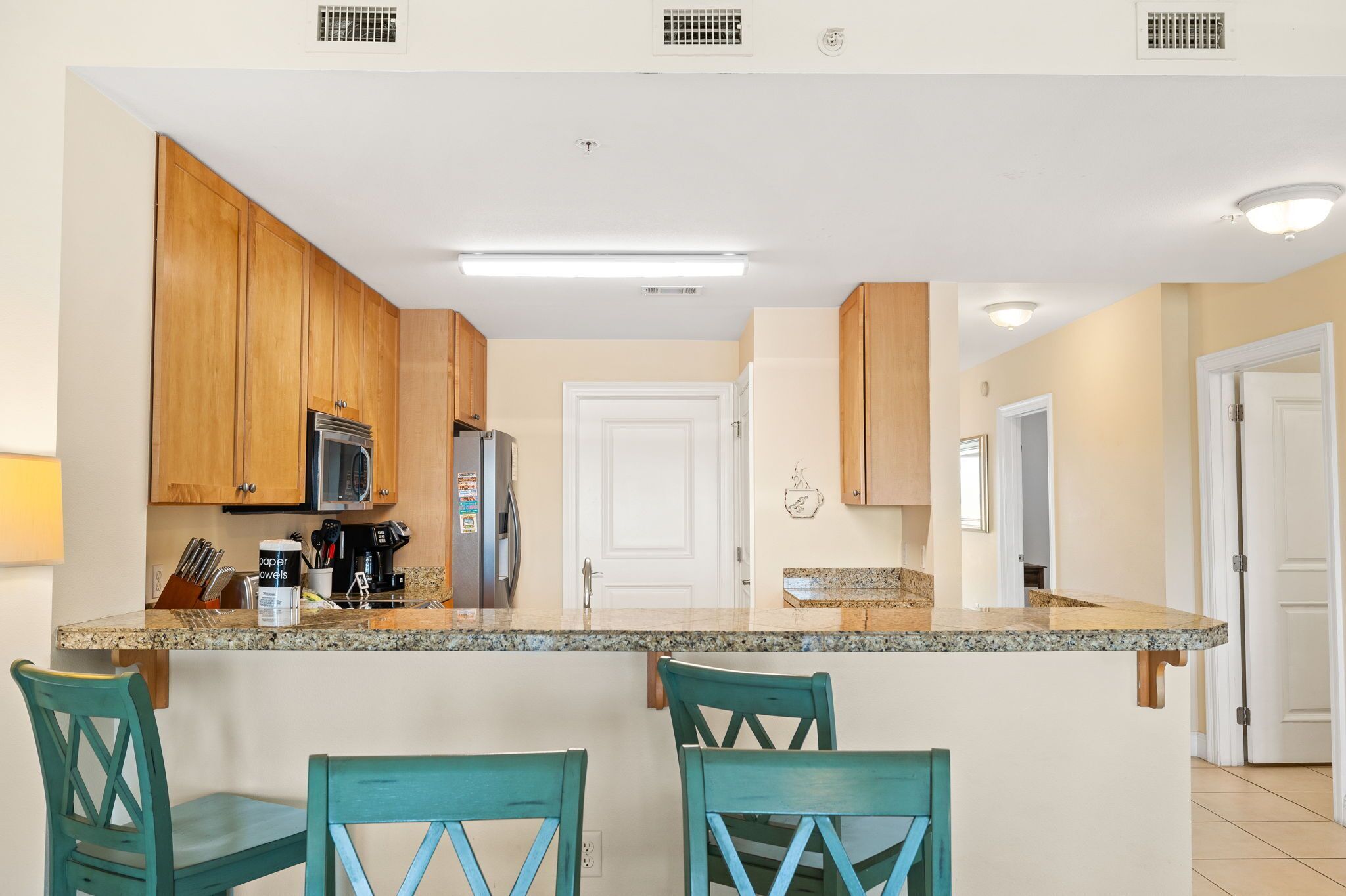 A kitchen with wooden cabinets, a granite countertop, and teal chairs.