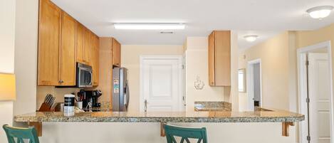 A kitchen with wooden cabinets, a granite countertop, and teal chairs.