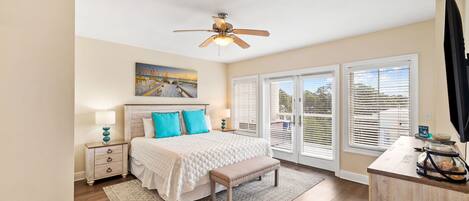 A bedroom with a bed, bedside tables, a bench, a ceiling fan, and large windows.