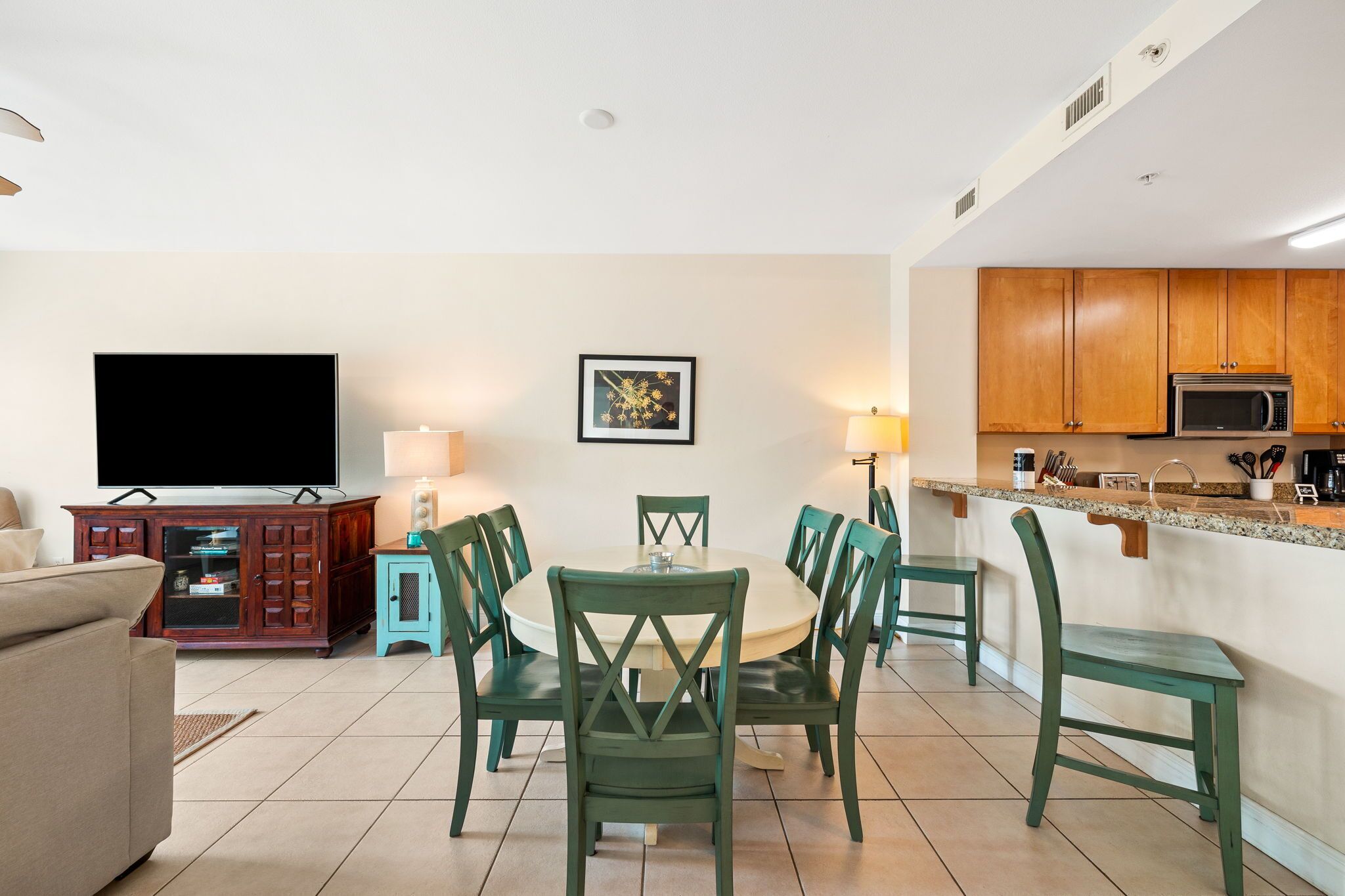 Una sala de estar con televisor, una mesa de comedor con sillas, una zona de cocina con armarios y un microondas, y un cuadro en la pared.