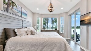 A bedroom with a large bed, a chandelier, a view of the outdoors, and a painting on the wall. - Naples lake view condo at Lely golf resort! (Naples)