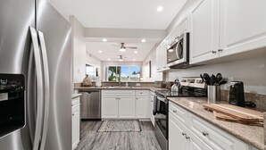A modern kitchen with stainless steel appliances, white cabinetry, and a view to the outdoors. - Naples lake view condo at Lely golf resort! (Naples)