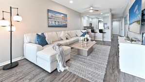 A modern living room with a sofa, coffee table, and a painting of a beach scene. - Naples lake view condo at Lely golf resort! (Naples)