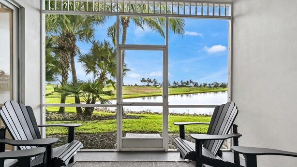 A balcony with two Adirondack chairs and a small table, overlooking a water body and palm trees. - Naples lake view condo at Lely golf resort! (Naples)