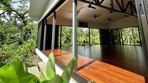 A modern interior with a wooden floor, ceiling fans, and large windows offering a view of lush greenery. - Nereus Retreats (Puerto Jiménez)