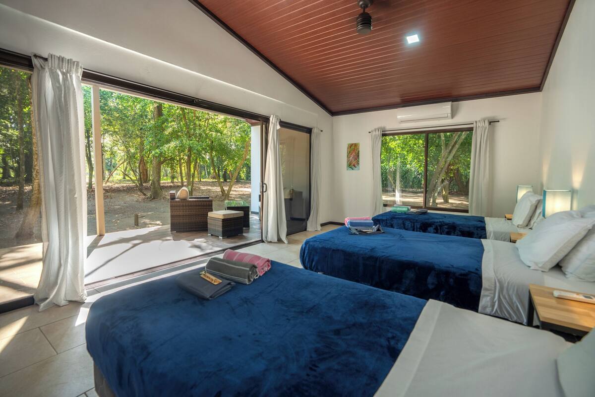 Ein Schlafzimmer mit zwei Betten, einem großen Fenster und Blick auf Bäume.