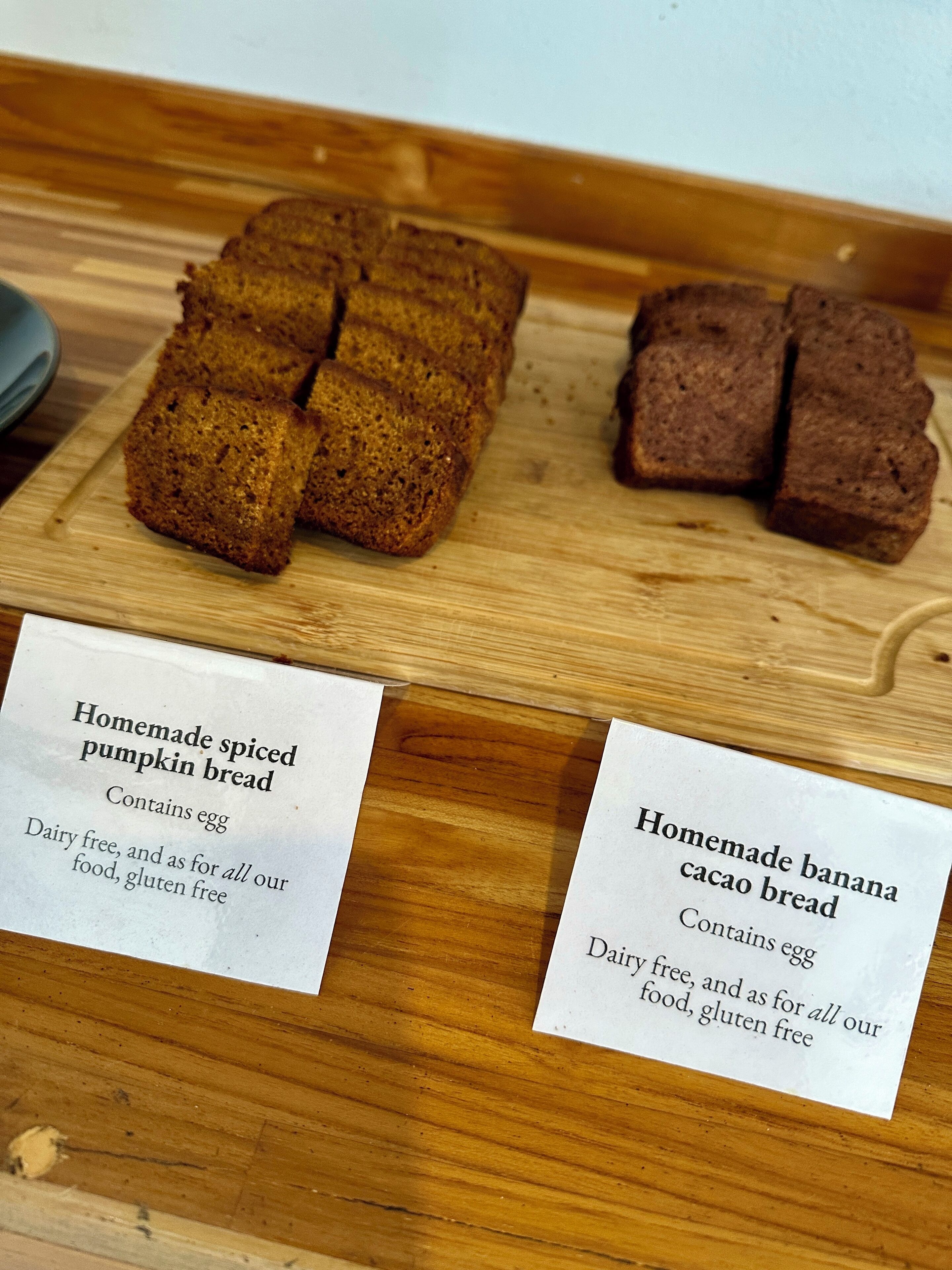 Dos tipos de pan casero sobre tablas de madera, con etiquetas que indican que son sin gluten ni huevo.