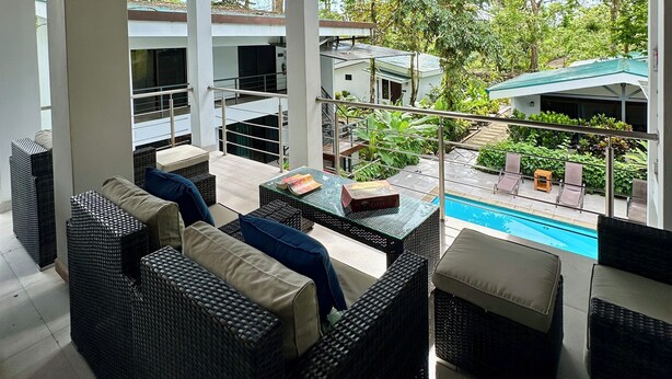 A covered outdoor seating area with wicker furniture and a pool in the background. - Nereus Retreats (Puerto Jiménez)