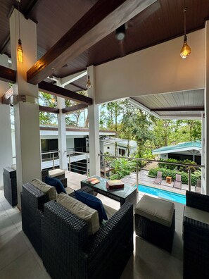 A covered outdoor seating area with wicker furniture and a pool in the background. - Nereus Retreats (Puerto Jiménez)