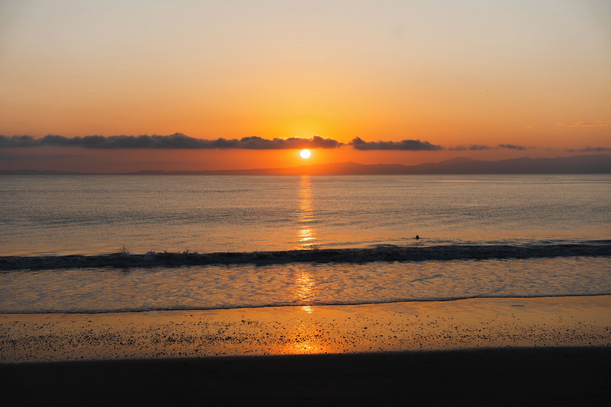 Un atardecer sobre un mar tranquilo con una playa al frente.