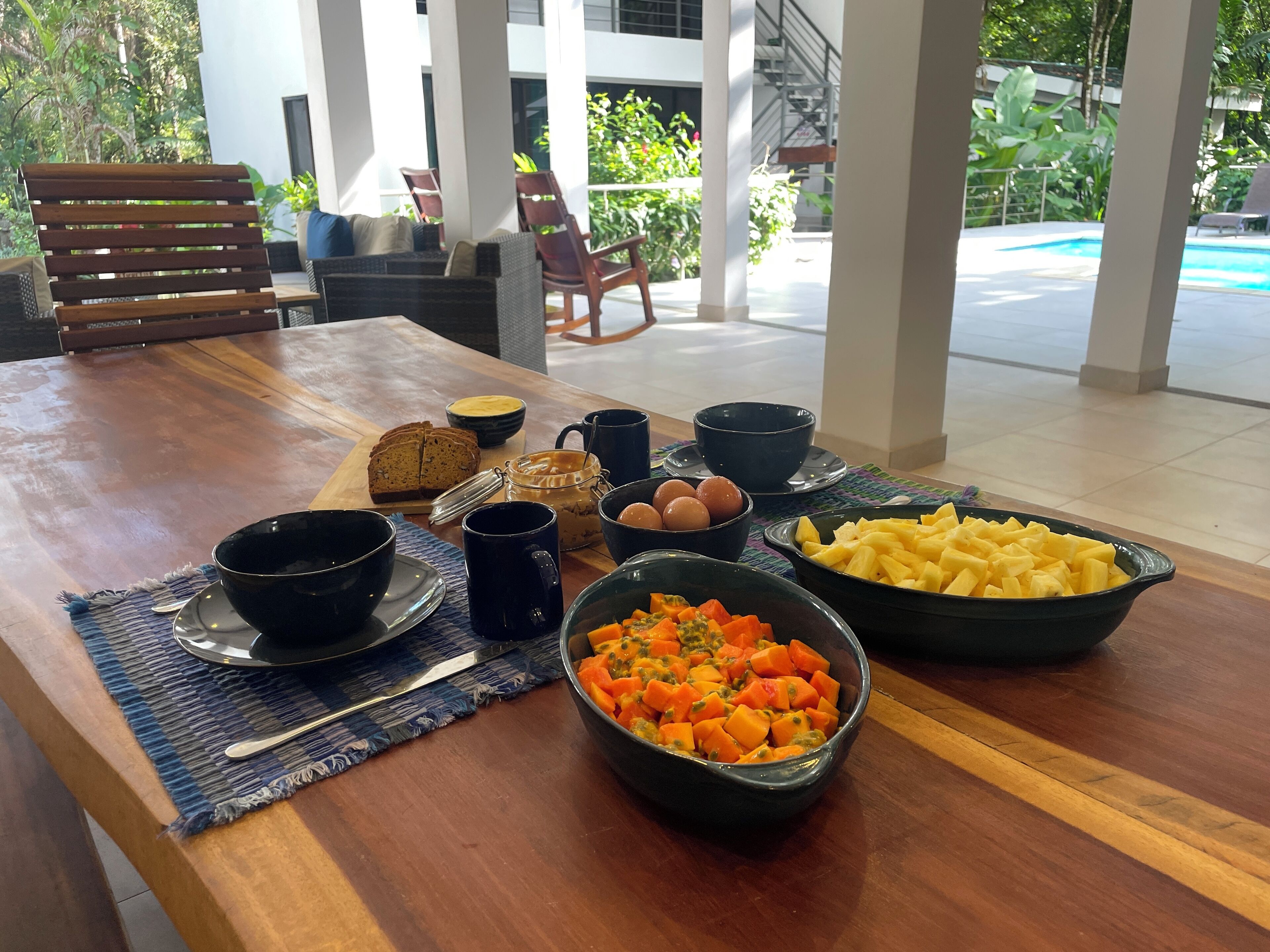 Une table de petit-déjeuner avec du pain, des œufs, des fruits et un bol de légumes.