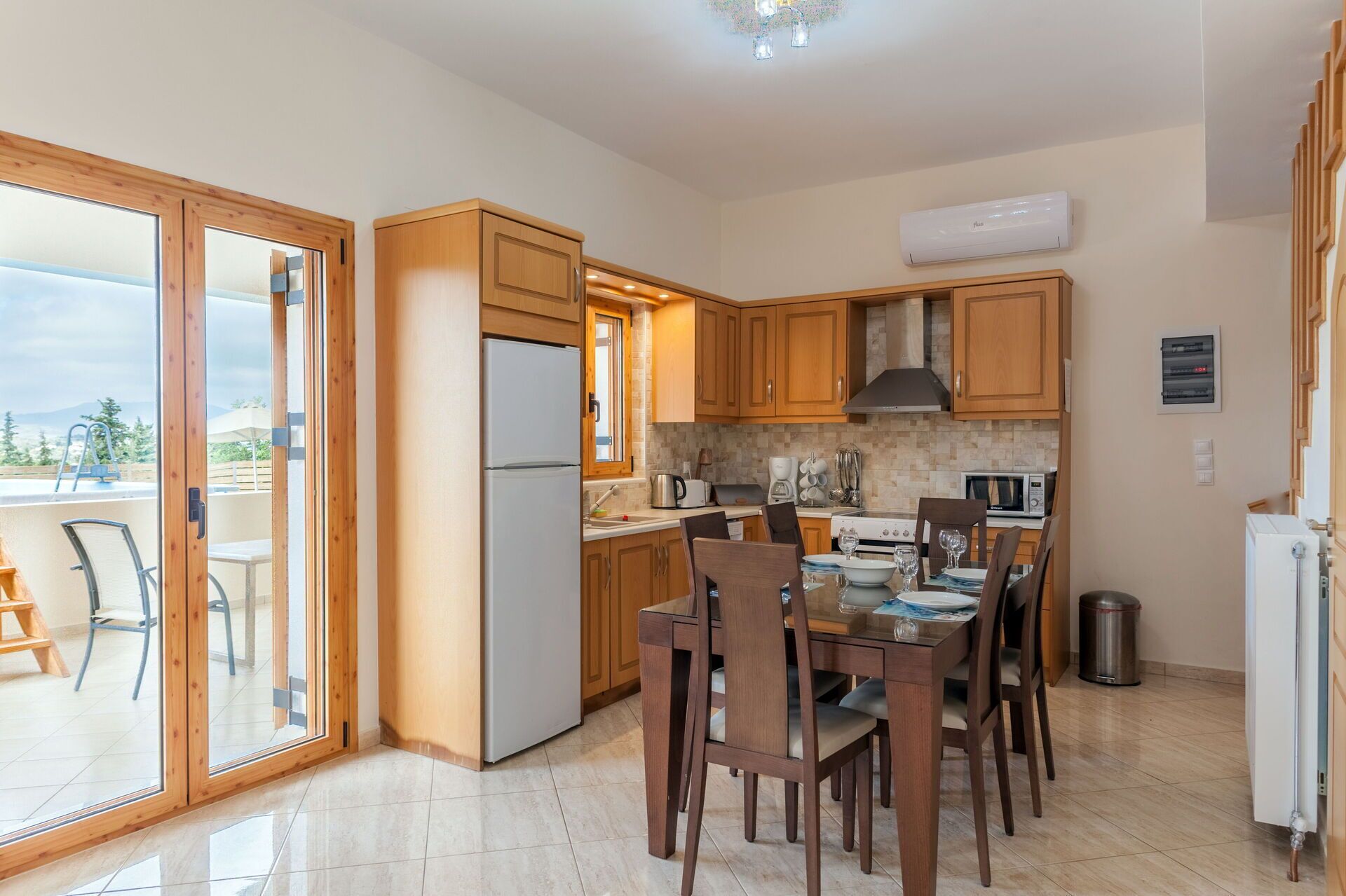 A modern kitchen with wooden cabinets, a refrigerator, and a dining area with chairs and a table.
