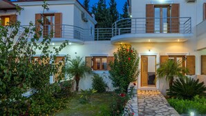 A two-story building with a balcony, a stone pathway, and a garden with various plants and flowers. - Villa Giorgos - Villa with private pool (Ágios Pávlos)