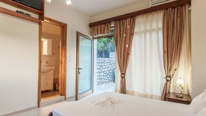 A bedroom with a bed, a TV, an air conditioner, and a bathroom with a sink and toilet. - Villa Giorgos - Villa with private pool (Ágios Pávlos)