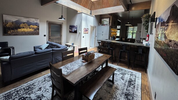 A modern kitchen with a central island, a dining area with a wooden table and benches, and a living room with a sofa and a large painting. - “The Roost” downtown Red Lodge, MT (Red Lodge)