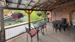 A covered outdoor patio with a wooden table and chairs, hanging flower baskets, and a brick wall. - “The Roost” downtown Red Lodge, MT (Red Lodge)