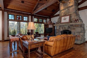 A cozy living room with a stone fireplace, leather furniture, and large windows overlooking a mountainous landscape. - 20 Peaks View (4-Bedroom Home) by Moonlight Basin Lodging by Moonlight Basin Lodging (Big Sky)
