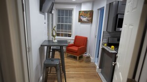 A narrow hallway with a dining table and chairs, a red chair, a window with blinds, and a kitchen area with appliances. - II New apartment with Luxury amenities in Boston (Boston)