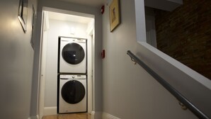 A laundry room with two stacked washers and dryers, a wooden floor, a white door, and a brick wall. - II New apartment with Luxury amenities in Boston (Boston)