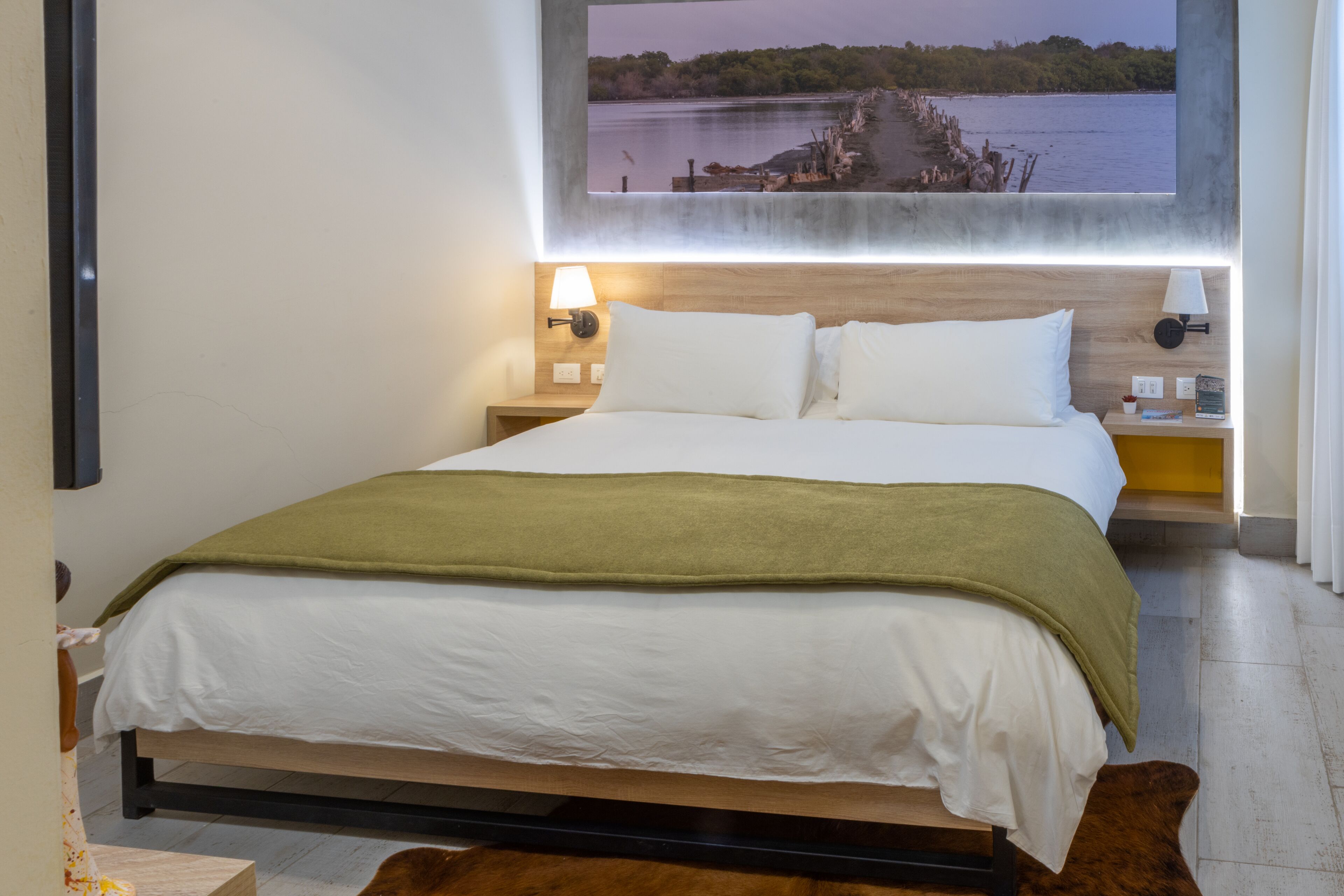 A modern hotel room with a large bed, wooden headboard, and a view of a lake through a window.