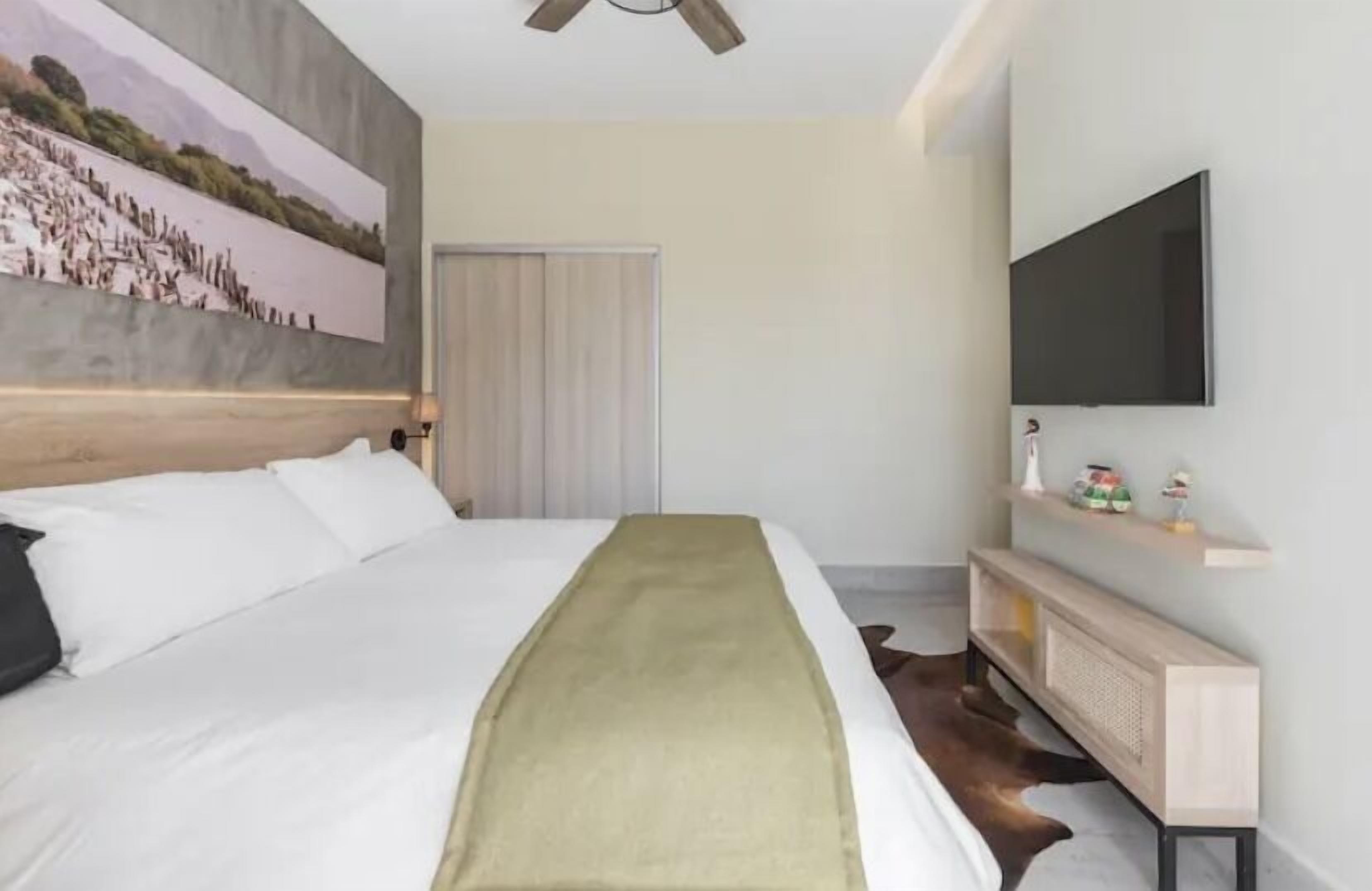 Una camera d'albergo moderna con un letto grande, una TV a parete e un quadro appeso.