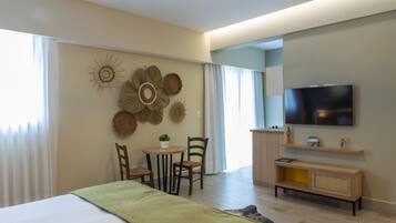 A modern hotel room with a bed, a dining area with chairs and a table, a television mounted on the wall, and decorative wall art.