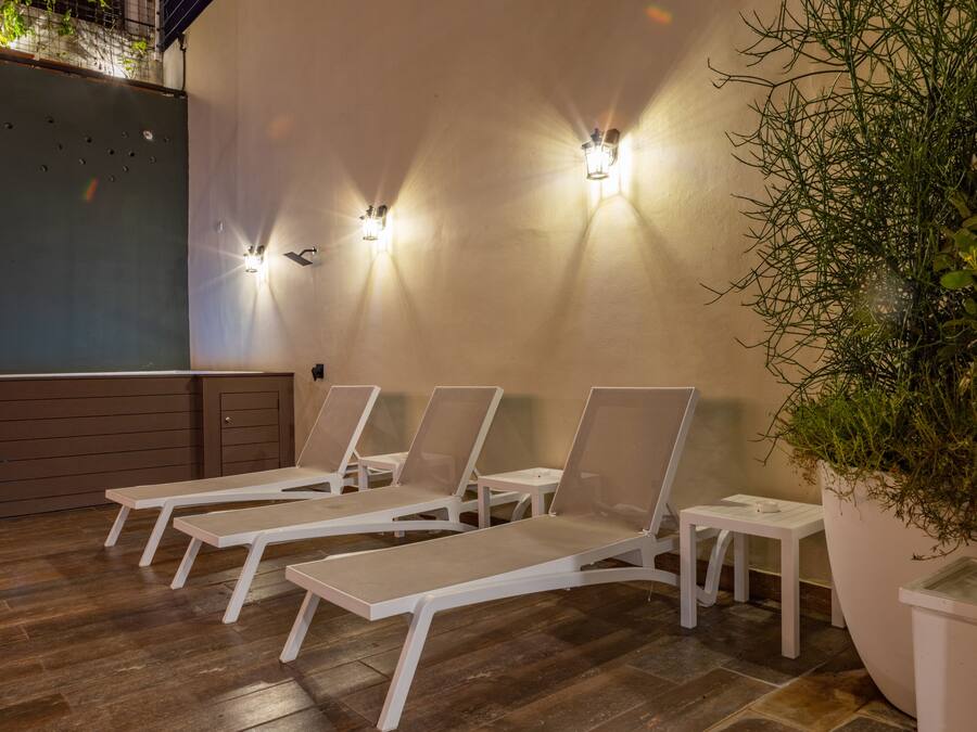 A sunlit outdoor seating area with lounge chairs and wall-mounted lights.