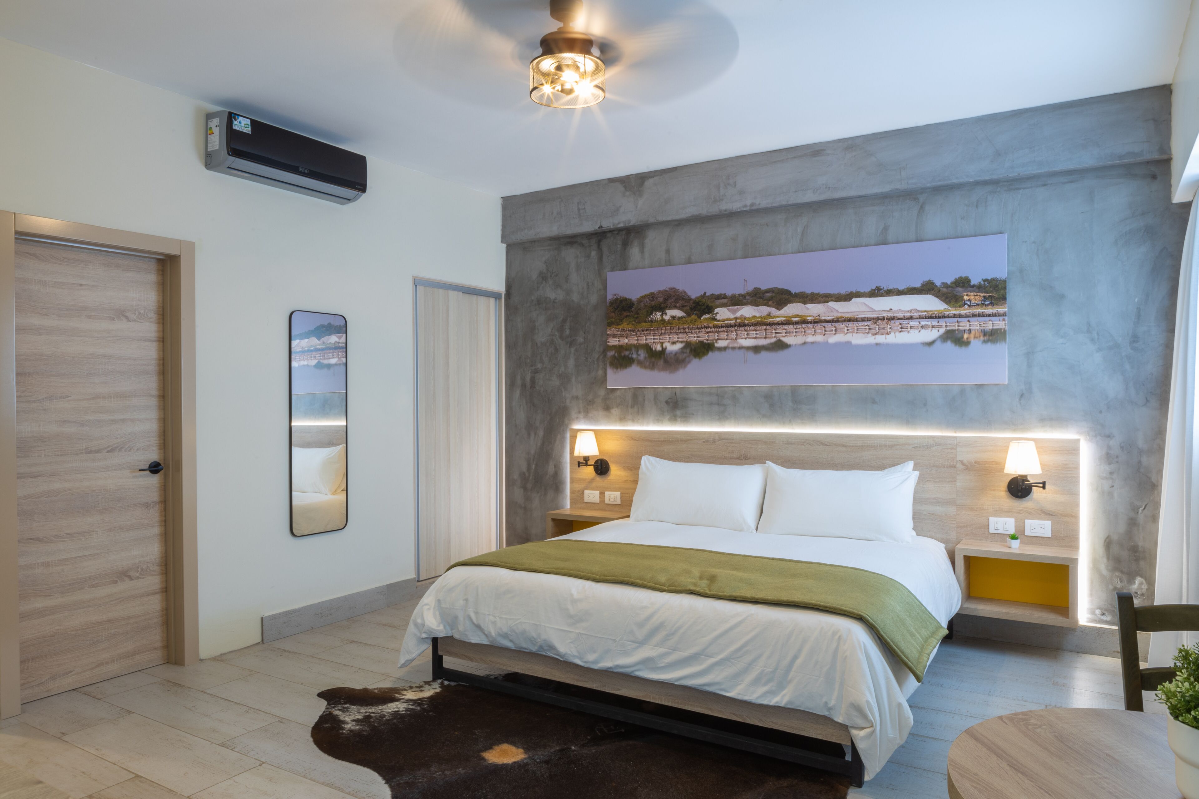 A modern bedroom with a large bed, a mounted artwork, a ceiling fan, and a small table with a plant.
