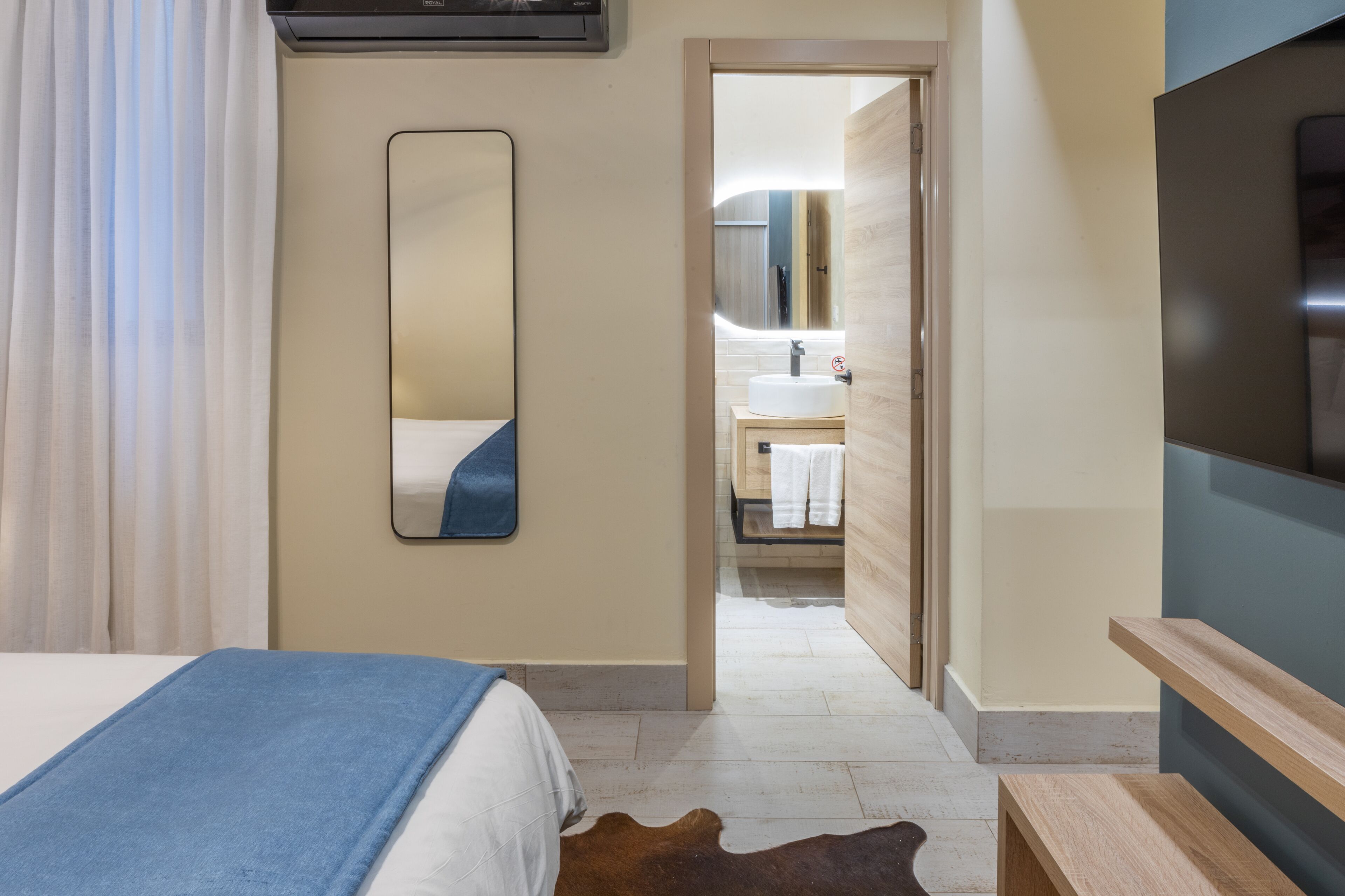 Habitación de hotel con cama, un espejo grande, televisor y baño visible a través de una puerta abierta.